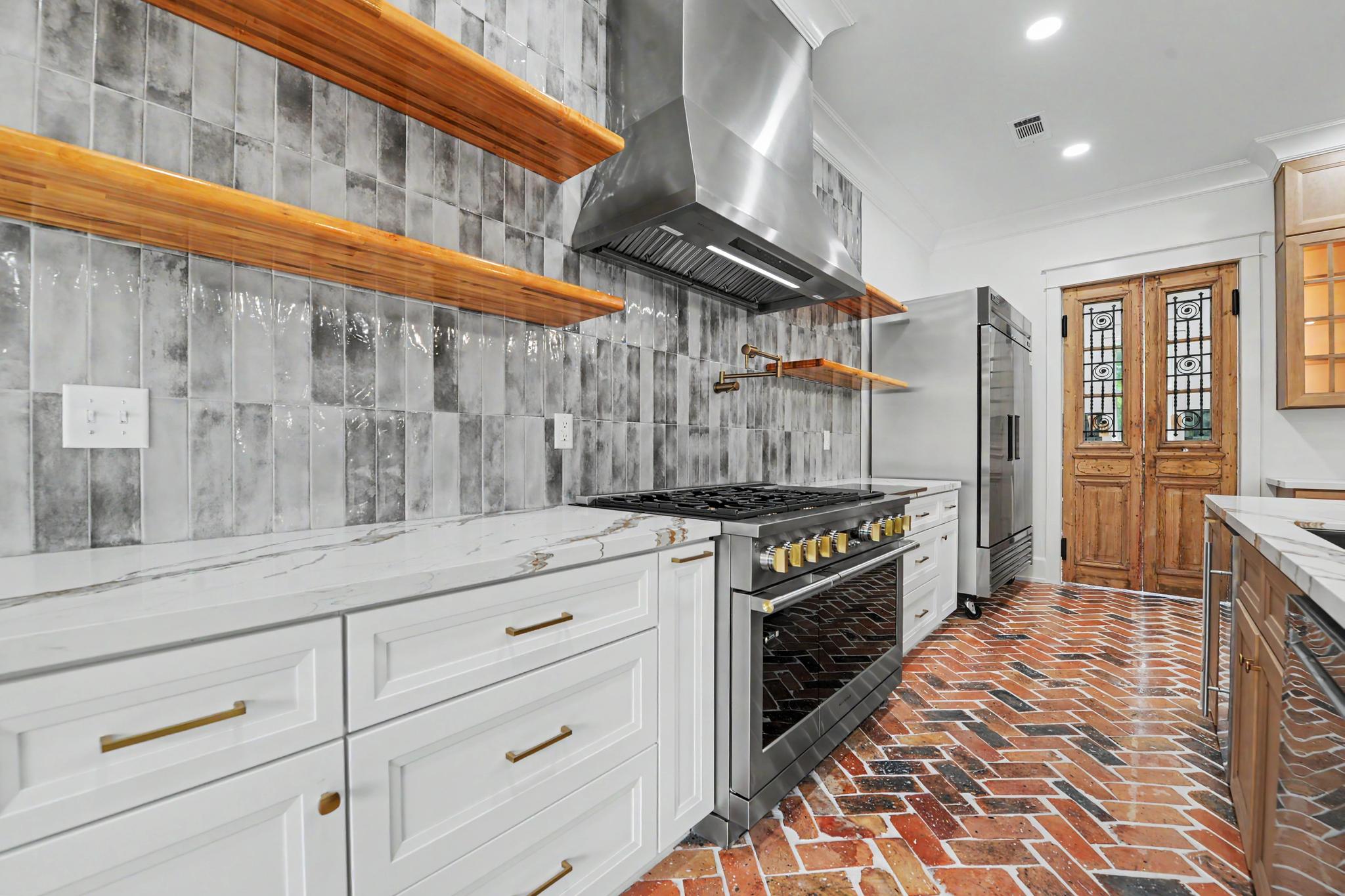 Custom kitchen with a professional gas range, stainless vent hood, and floating wood shelves by Full Armour Homes